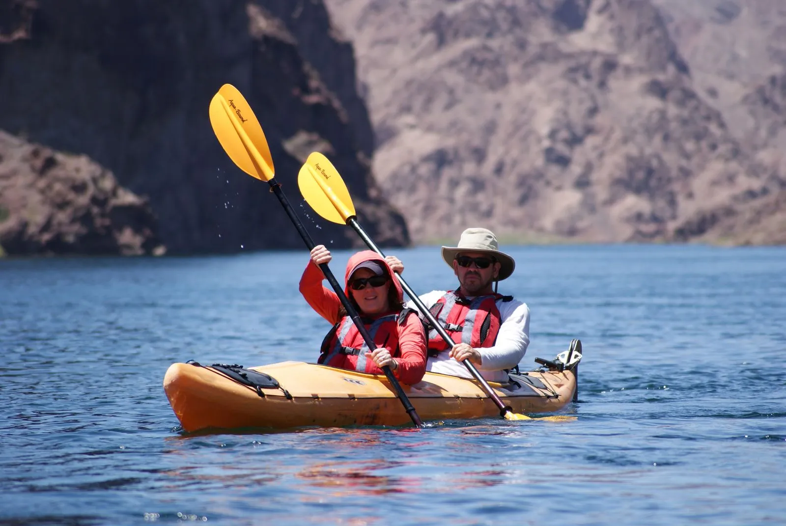 A relaxed first-time paddler smiling mid-stroke on calm, flat water, mountains in the background - conveys "this is easier than you think (Source: Evolution Expeditions)